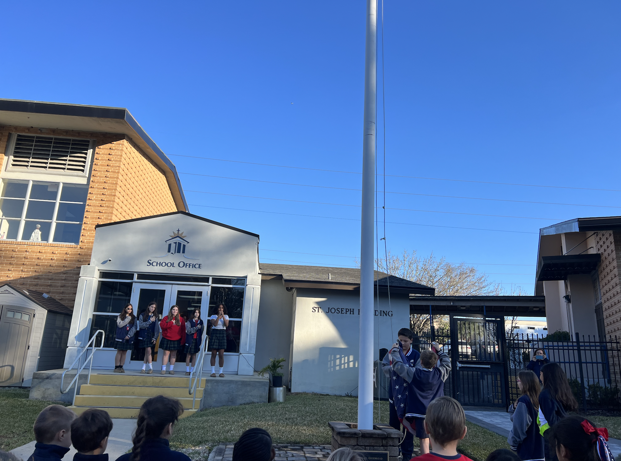 Image of students around the flag pole as a student puts the flag on
