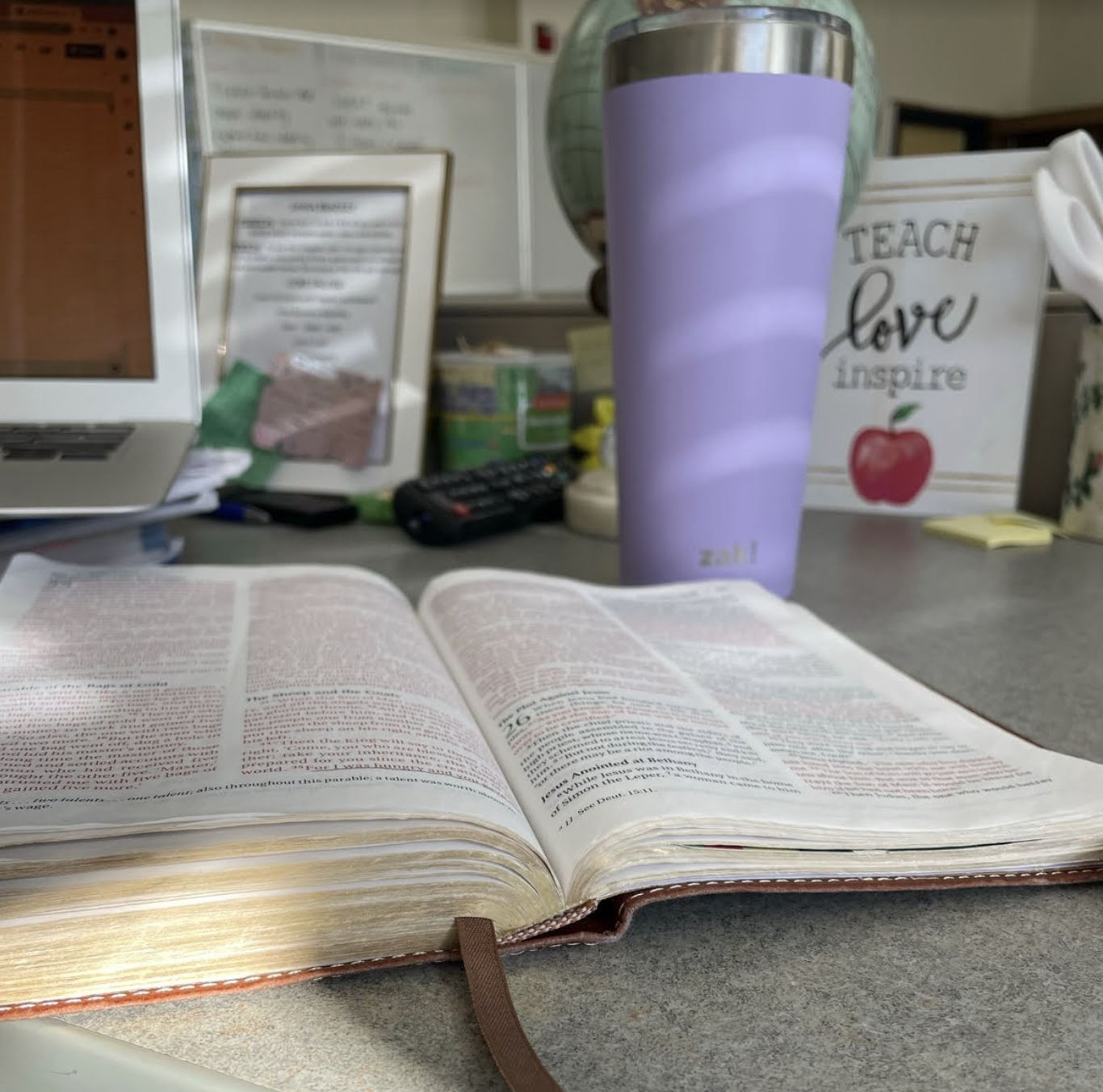 Image of a Bible open on a desk with a purple cup in the background