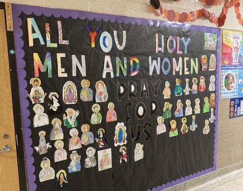 Image of a bulletin board with wording that says "All You Holy Men and Women" with images of saints below it.